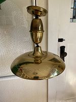 Close-up photo showing the polished brass dome-shaped light shade with detailed scalloped perforation pattern around the edge and brass ceiling mount.