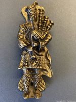 Front view of vintage solid brass door knocker depicting Scottish man playing bagpipes, showing detailed attire and figure.