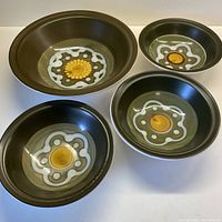Photo showing all four bowls arranged with one large serving bowl and three smaller cereal bowls displaying the olive green, mustard, chocolate, and cream color scheme and circular pattern in the center.