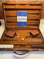 Full view of backgammon board inside open case with dice cups, dice, and instruction booklet laid out