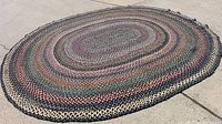 Full view of large oval braided rag rug laid flat on concrete, showing its size and shape.