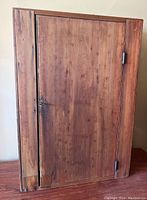 Front view of the wooden hanging cabinet showing the single door with metal latch and hinges.