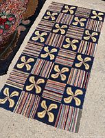 Photo showing antique hooked rug laid flat on concrete with alternating blocks of pinwheel and striped patterns.