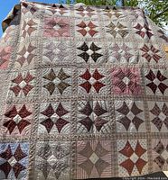 Full view of the antique patchwork quilt showing multiple blocks with star-like patterns in brown, pink, and cream tones.