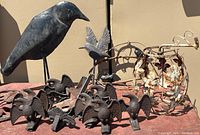 Cast iron snow bird statues and contemporary tin crow grouped together on a surface against a beige wall.