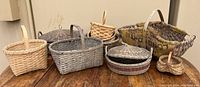 Seven assorted baskets on a wooden table, view showing large burlap-lined basket, round lidded basket, and smaller basket with divided sections.