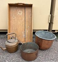 Photo showing copper kettle, two copper pots in front, and wooden tray leaning against background