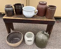 Photo showing all eight crocks including ceramic and stoneware jugs and bowls arranged on and under a wooden bench