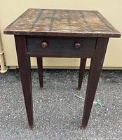 Front view of folk art painted side table showing one drawer with wooden knobs and tapered legs.