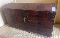 Front view of large wooden trunk with handwritten lettering and metal lock hardware.