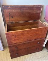 Front view of wooden lift top blanket chest with open lid revealing interior and two drawers below with wooden knobs.