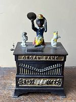 Front view showing “ORGAN BANK” lettering, decorative front grille and figure with cymbal and two dogs