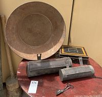 Photo of antique painted toleware box, two hanging candle boxes, large white metal sieve, and a metal scissors-like tool on a red table.