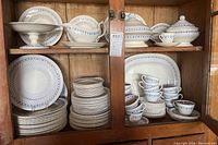 Photo showing stacked plates, cups, saucers, covered tureens, and footed bowl inside wooden cabinet.