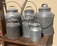 Six galvanized metal dairy pails with lids and bail handles displayed on wooden table