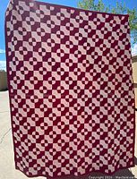 Full view of the vintage quilt hanging outdoors showing the red and pink patchwork pattern in a geometric design.