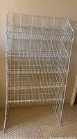 Front view of white wire folding magazine display shelf showing three angled wire basket tiers and folding frame