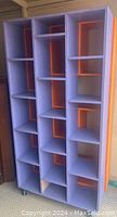 Large handcrafted shelving unit painted purple with orange interior compartments, shown front on in natural light.