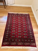 Red wool Bokhara-style area rug with geometric medallions and fringe laid on hardwood floor