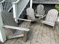 Four wooden Adirondack chairs arranged on a brick patio, showing weathered gray wood with visible wear from outdoor exposure.
