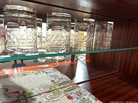Four clear glass highball glasses arranged on a glass shelf inside a wooden cabinet