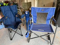 Three camping chairs in blue and olive green colors arranged in a garage; two are unfolded showing seating area and armrests with metal frames.