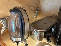 Glass electric kettle with black handle and stainless steel base, stainless steel fish steamer, and two silver fish-shaped serving plates visible