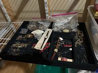 Tray containing assorted costume jewelry pieces, watches, and a small white pouch