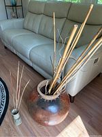 Photo showing the full view of the large floor pot with bamboo stalks and the smaller ceramic vase with cat tails placed beside it on the floor in a living area.