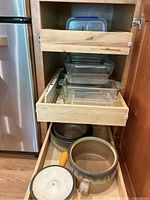 Lower kitchen cabinet drawer with brown ceramic cookware and Le Creuset ceramic sauce pot with lid, handle visible