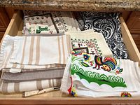 Drawer containing multiple folded dish towels with various patterns including stripes, floral, animal prints and paisley.
