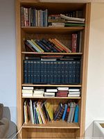 Full view of bookshelf with a variety of books arranged across five shelves including religious texts and secular works.