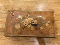 Closed rectangular burled wood music box with inlaid floral and violin design on the lid.