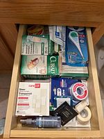 Image showing a drawer containing multiple first aid supplies such as bandages, medical tape, a thermometer, and other medical-related items.
