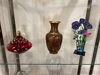 Red glass covered dish, red cloisonné vase, purple metal flower sculpture shown on glass shelf
