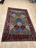 Red wool area rug with multicolor leaf and diamond shapes on a light wood floor