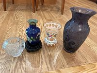 Photo showing four glass vases of different colors and designs on wood floor.