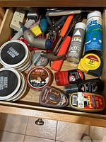 Drawer filled with various shoe care tins and spray cans, along with multiple hand tools including pliers, screwdrivers, and measuring tape.