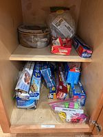 Inside cabinet showing two ceramic cooking dishes, multiple aluminum foil and plastic wrap boxes, and several clips in packaging.