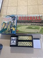 Photo showing Wizard's Quest and Baseball board game boxes next to an open dominoes set in a black leather case with domino tiles, score pad, and pencil.