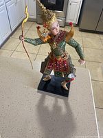 Full view of the Bangkok Thailand doll wearing a detailed traditional costume and holding a bow, standing on a black base.