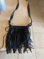 Front view of the black leather fringe purse showing the long fringe hanging down and the adjustable shoulder strap.