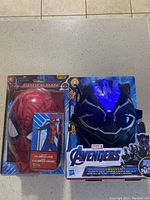 Two Marvel masks in original packaging: Spider-Man full jump suit mask and Black Panther Vibranium mask with LED light on forehead.