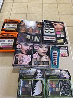Top-down photo of all boxed Halloween makeup kits and accessories arranged on beige floor. Shows packaging with images of models, brand names, and visible product components through clear plastic on some boxes.