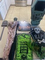 Photo of various Halloween decorations including a green coffin prop, tombstone signs, skeleton figures, and Halloween themed fabric hanging sign.