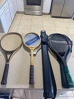 Three tennis racquets laid out on a kitchen counter next to a black pool cue case.
