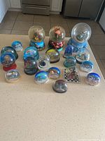 Full view of the 20 assorted snow globes on a countertop showing variety in size, theme, and base colors.