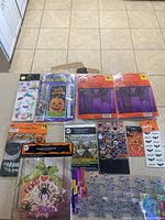 Full lot arranged on floor showing various Halloween decorations still in original packaging including door cover, masks, witch hats, sticker sheets, and window clings.