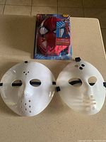 Spider-Man mask and jumpsuit set new in blister packaging alongside two used white plastic Jason masks