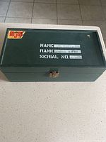 Top view of the green metal GI Joe locker with name, rank, and serial number stenciled in white and GI Joe sticker on the corner; shows some scratches and wear on surface.